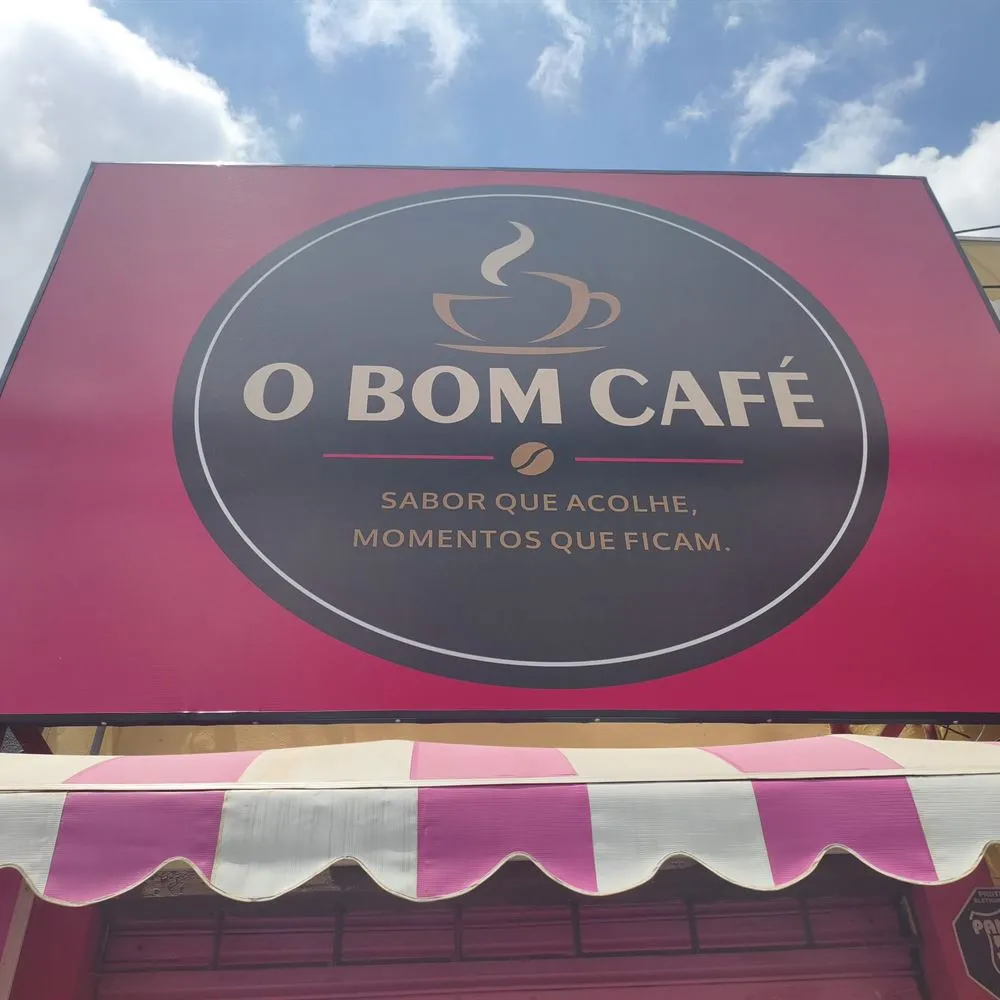 Fachada do O Bom Café: placa rosa com a logo e toldo listrado em rosa e branco