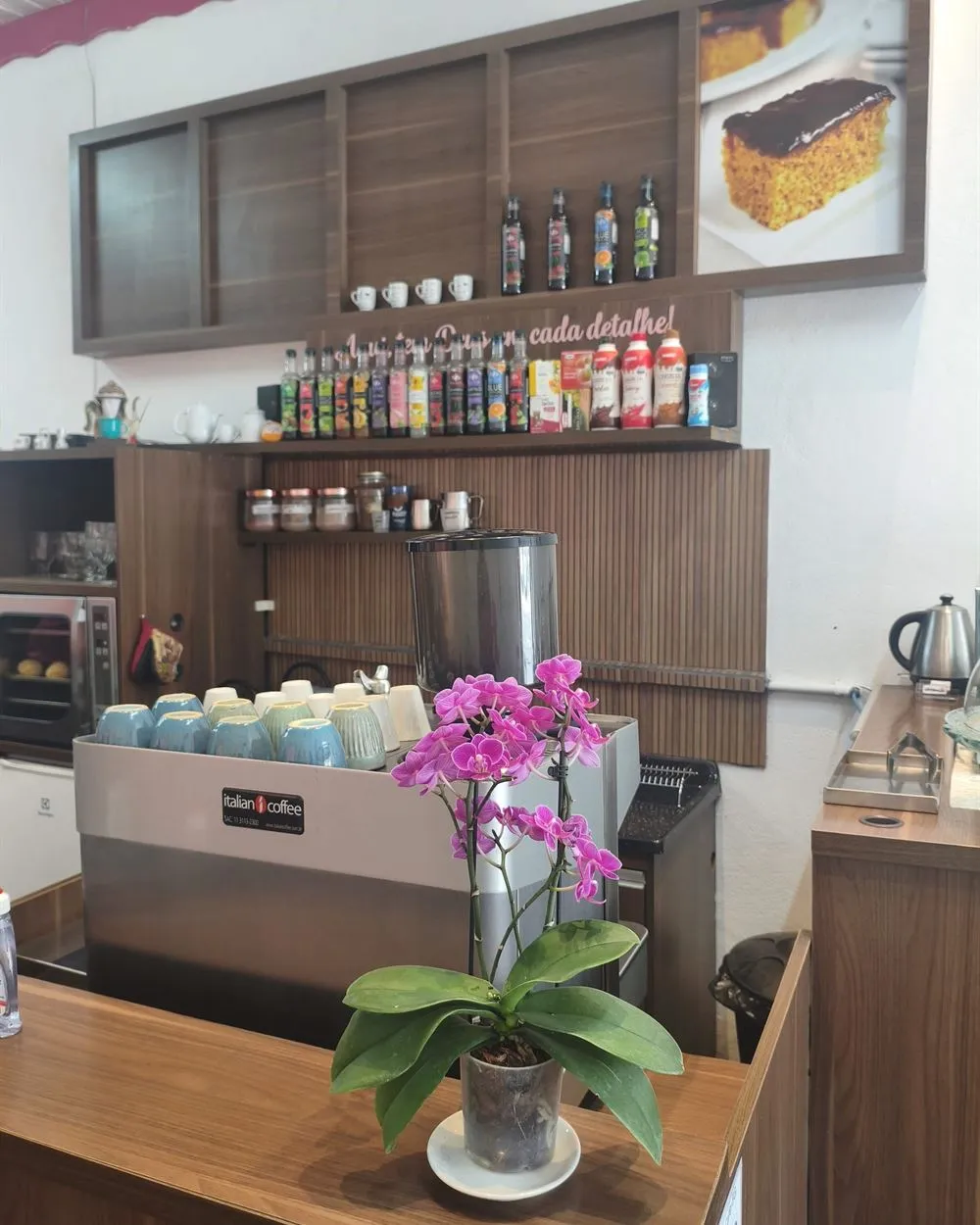 Balcão do O Bom Café com máquina de expresso, xícaras, xaropes e uma orquídea