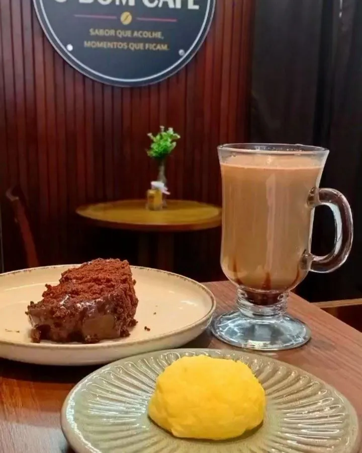 Chocolate quente, fatia de bolo e pão de queijo servidos na mesa